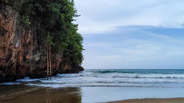 A beach with a rocky cliff and a ladder leading up to it. - VIVE EL VALLE Hotel (Samaná)