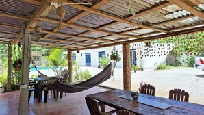 A covered outdoor area with a table and chairs, a hammock, and hanging plants. - VIVE EL VALLE Hotel (Samaná)