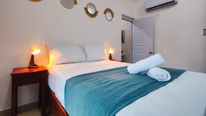A neatly made bed with a teal blanket, two bedside lamps, and three wall-mounted mirrors. - VIVE EL VALLE Hotel (Samaná)