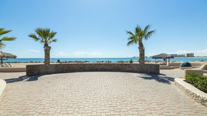 A paved patio area with palm trees, a stone wall, and beach views.