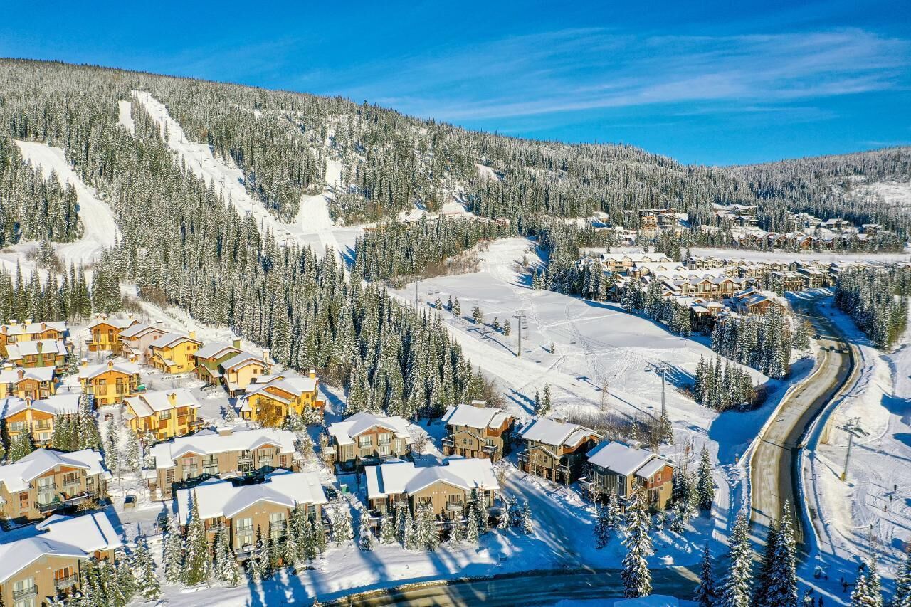 Et skisportssted dækket af sne med flere hytter, skiløjper og et bjergrigt landskab i baggrunden.