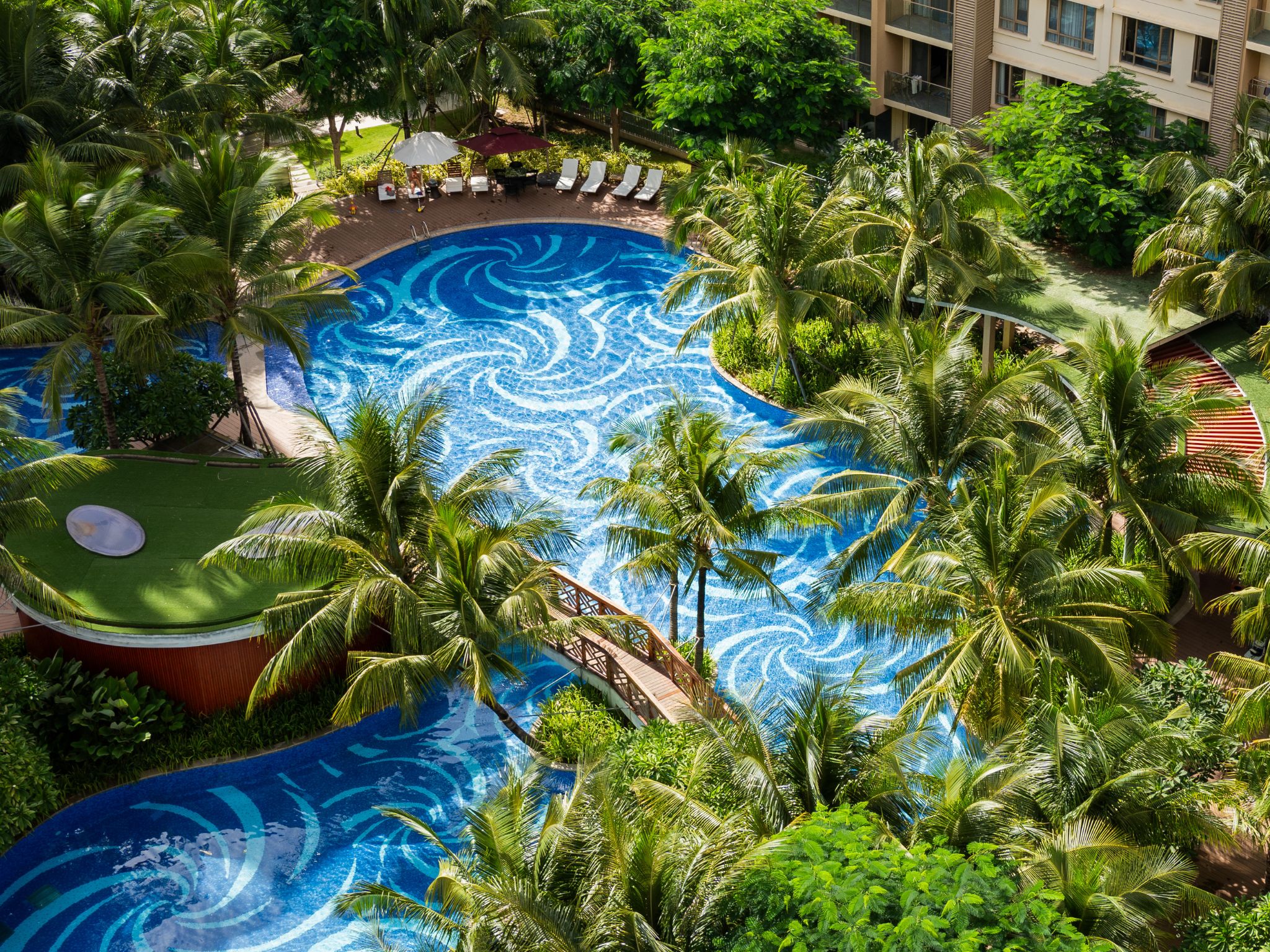 A large, multi-level swimming pool surrounded by lush greenery and palm trees.