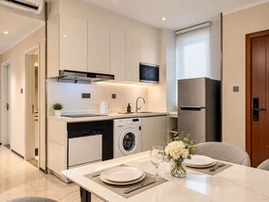 A modern kitchen with a dishwasher, microwave, and refrigerator. There is a dining table set with plates, a glass, and a vase with flowers.