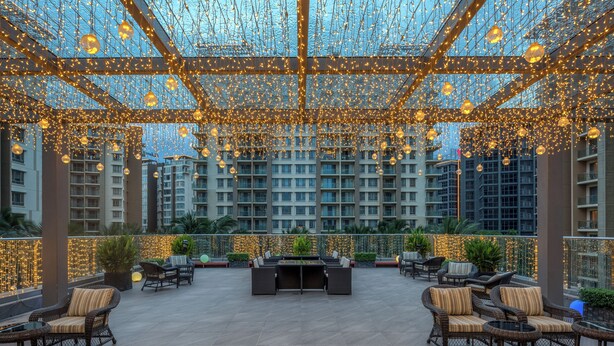 An outdoor lounge area with wicker furniture, a central table, and a view of high-rise buildings. - Soladia Hotel & Residences by One Park (Phnom Penh)