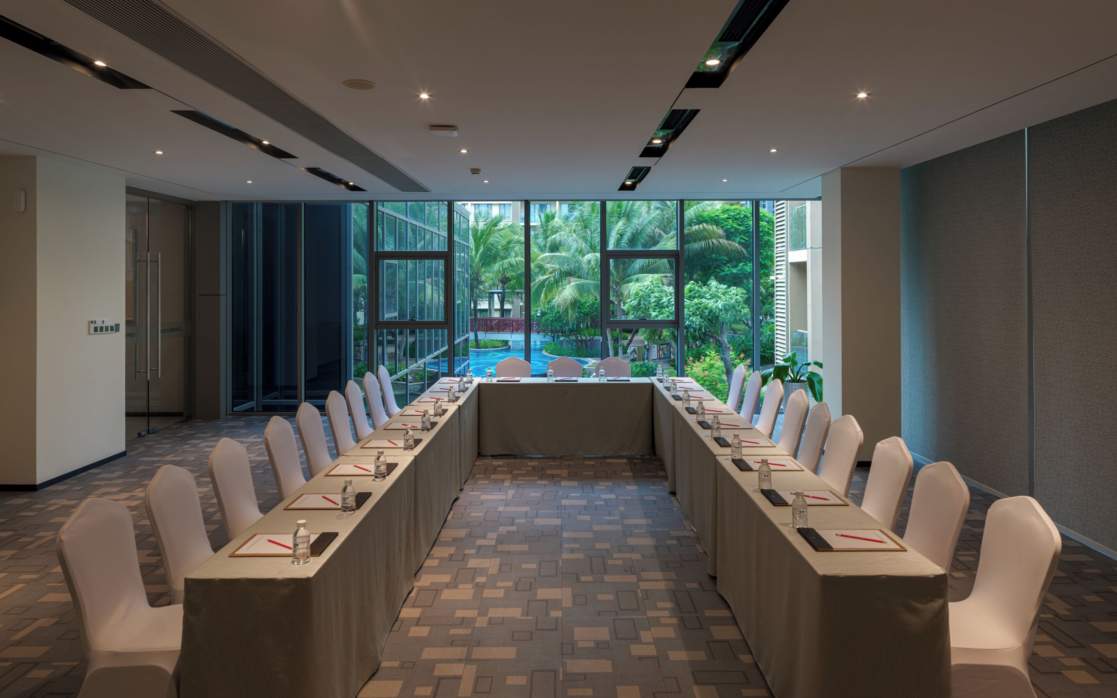 Ein Konferenzraum mit einem langen Tisch, Stühlen und Blick auf Pool und Grünflächen.