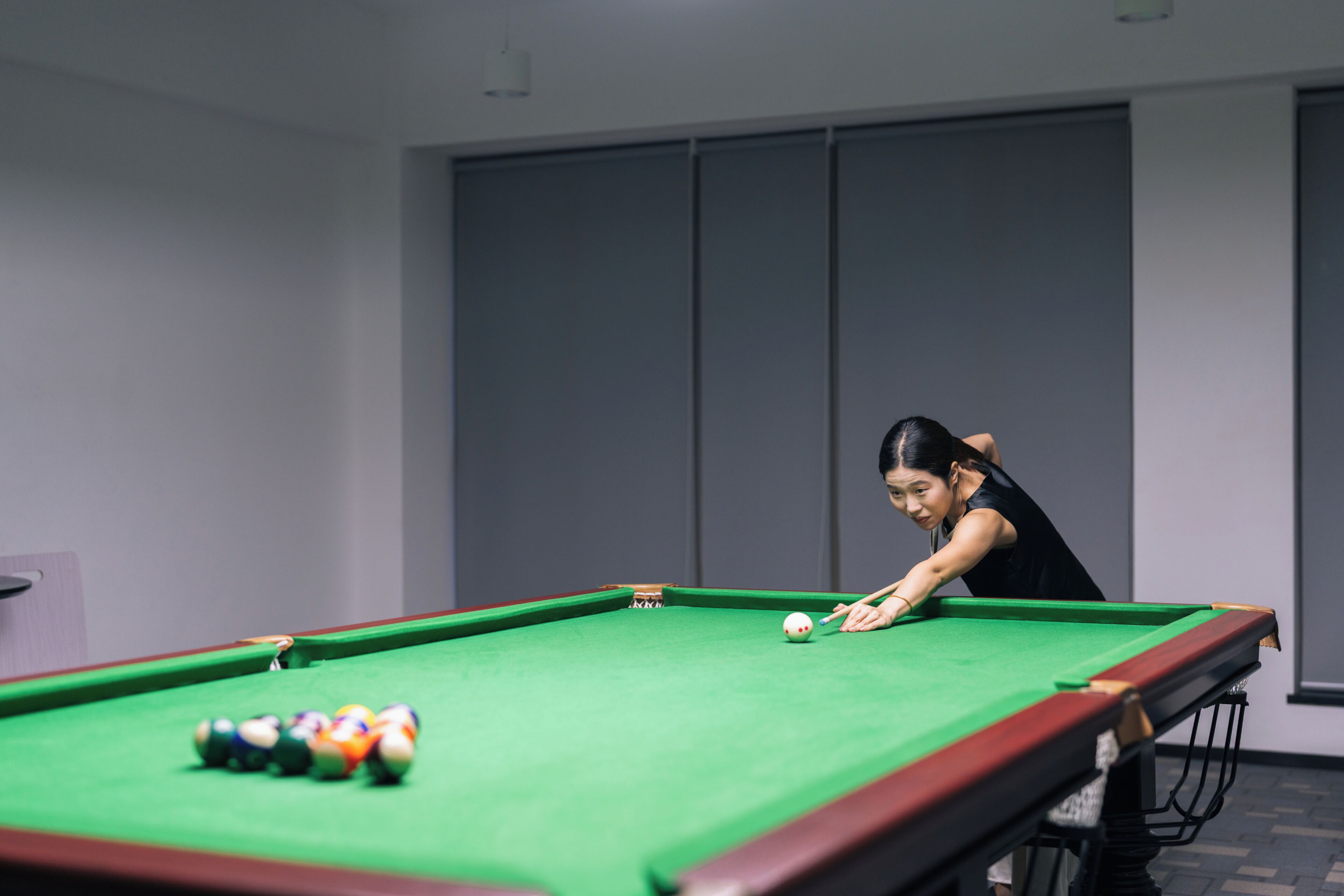 Une table de billard avec des billes, une personne qui joue, et un mur uni avec une porte.
