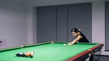 Une table de billard avec des billes, une personne qui joue, et un mur uni avec une porte.