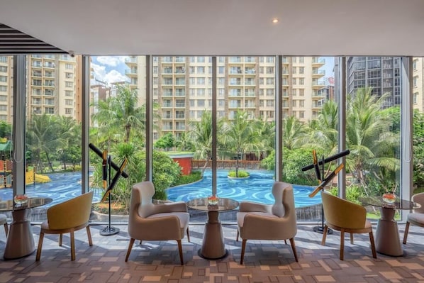 A hotel room with large windows, a pool view, and modern furniture.