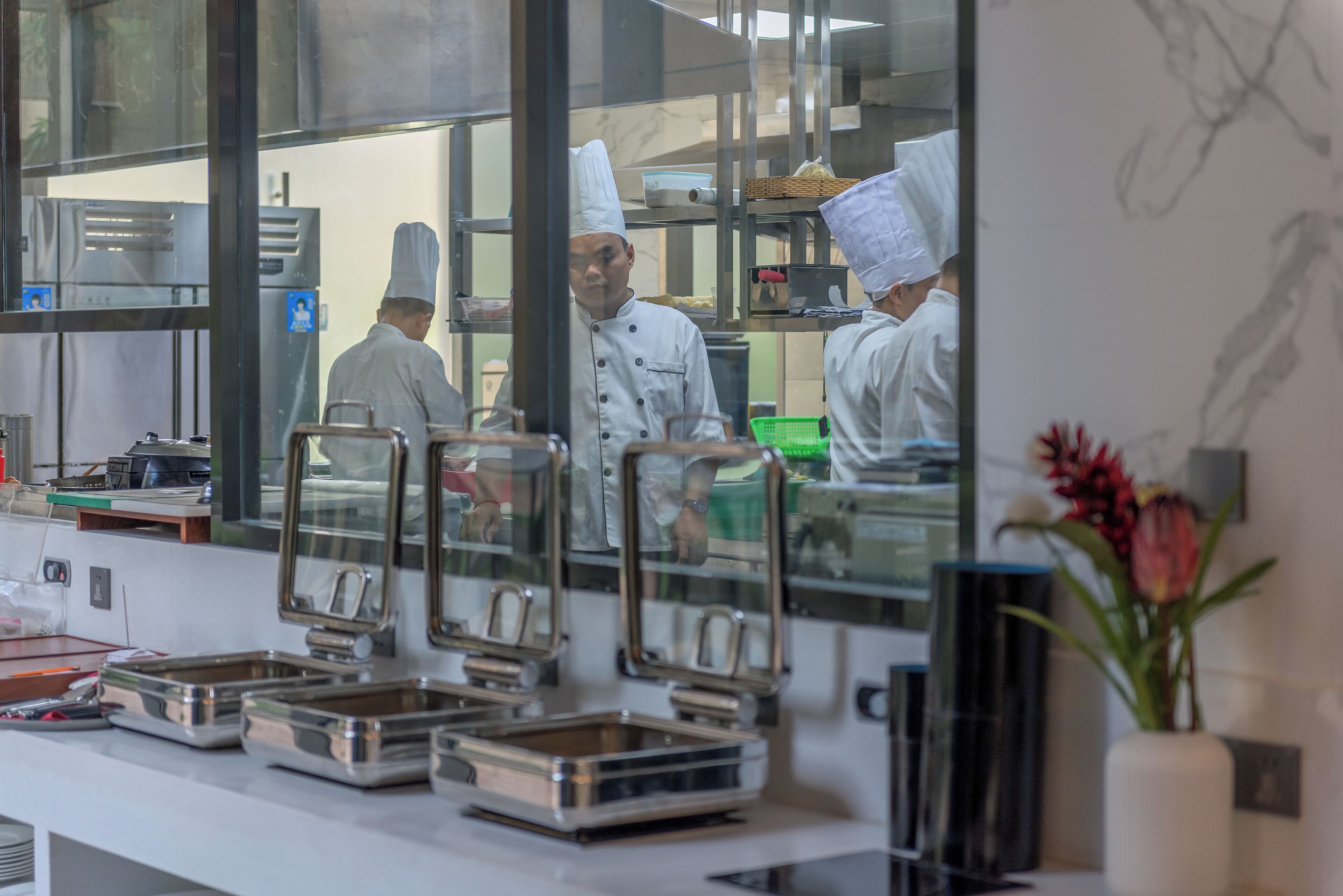 A kitchen with chefs in white uniforms and hats, stainless steel appliances, and food service equipment.