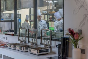 A kitchen with chefs in white uniforms and hats, stainless steel appliances, and food service equipment.