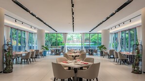 A spacious dining area with multiple tables and chairs, large windows with curtains, and potted plants. - Soladia Hotel & Residences by One Park (Phnom Penh)