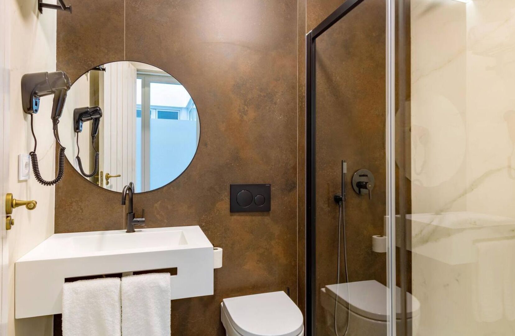 A bathroom with a white sink, a round mirror, a toilet, and a shower area.