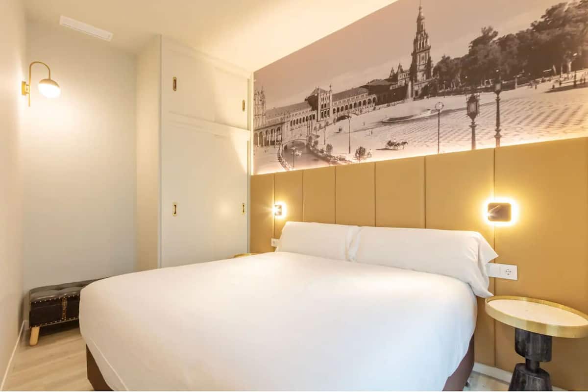 A hotel room with a large bed, a wall-mounted picture of a historic building, and two bedside lamps.