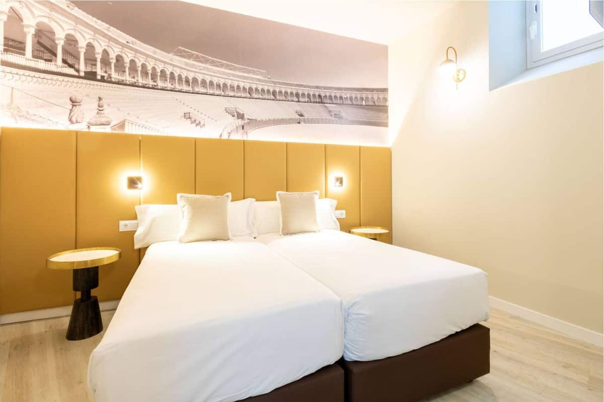 A hotel room with a large bed, two bedside tables, and a mural of a stadium on the wall.