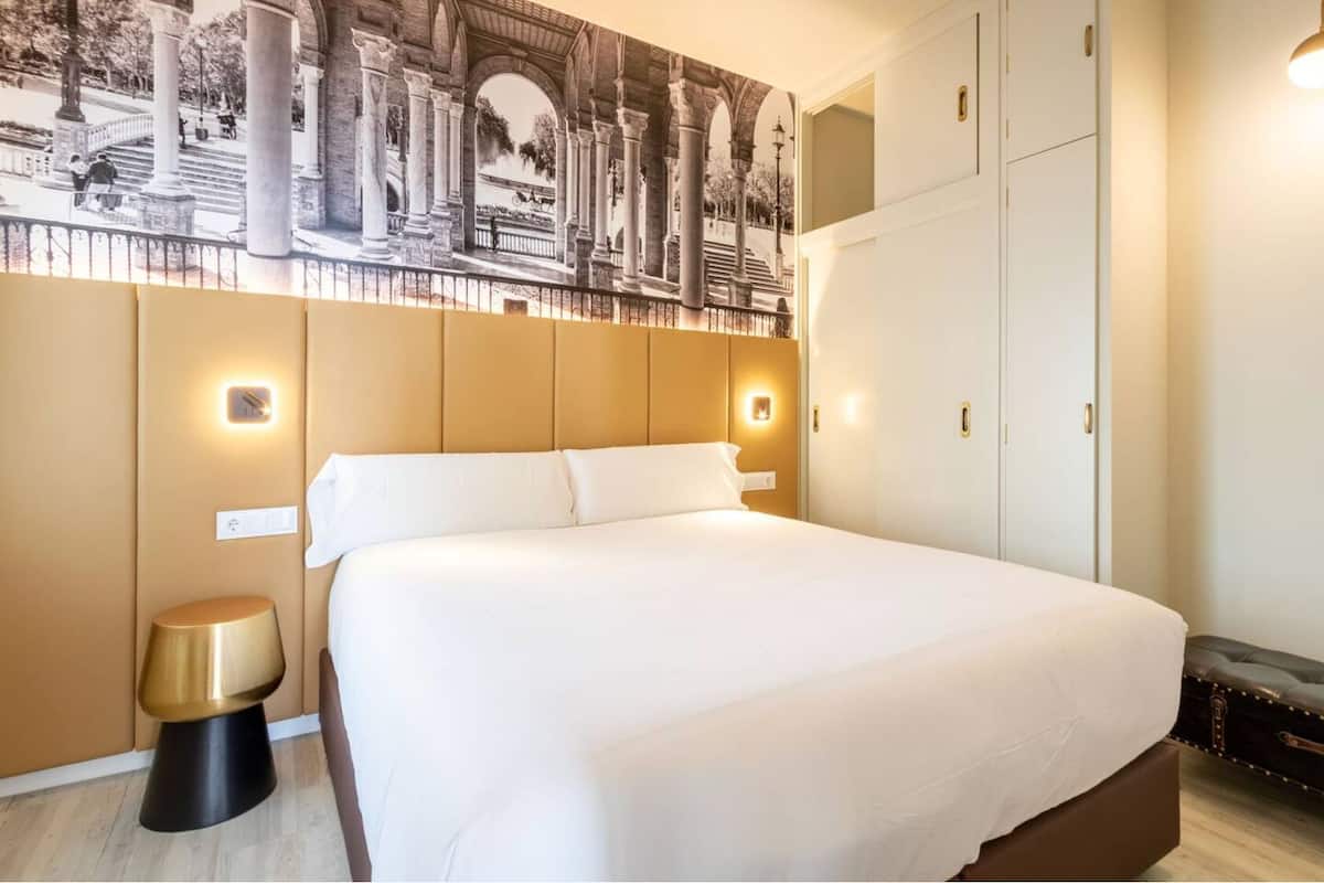 A large bed with a headboard, a bedside table, and a wall-mounted light.