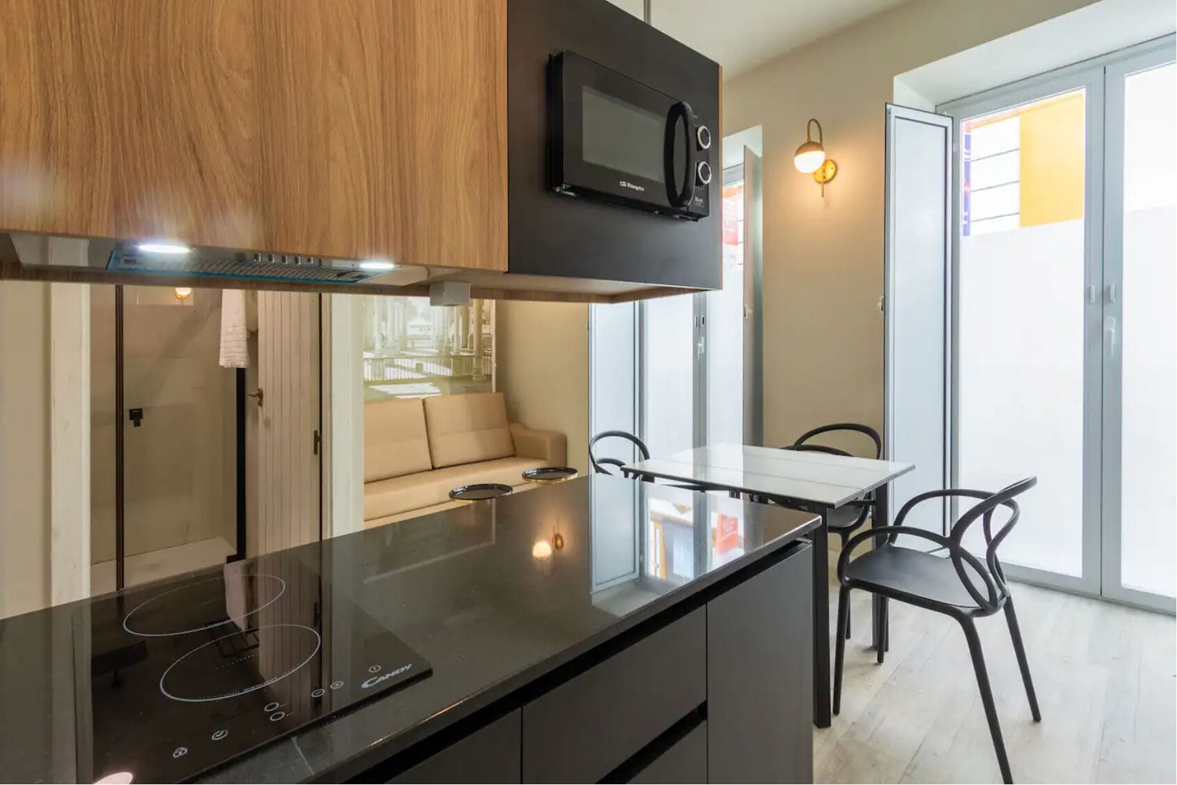 A modern kitchen with a black countertop, a microwave, and a glass door leading to a balcony.