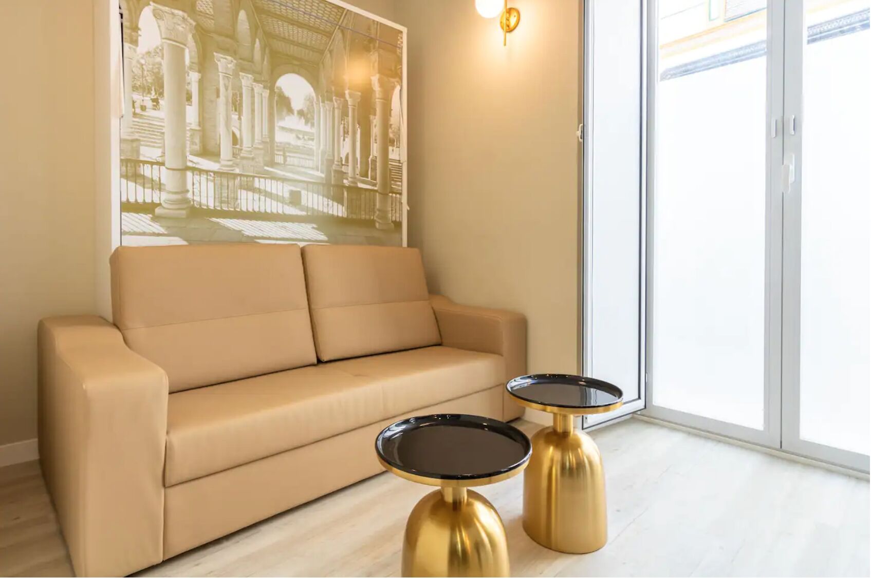 Egy modern nappali, melyben bézs színű kanapé, két arany és fekete színű dobozasztal, valamint egy nagyméretű, keretezett kép látható, mely egy klasszikus épületet ábrázol.