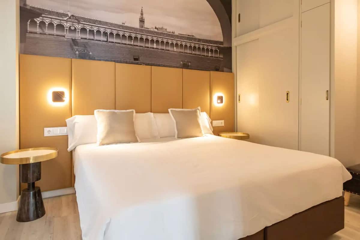 A hotel room with a large bed, two bedside tables, a wall-mounted TV, and a view of a historic building.