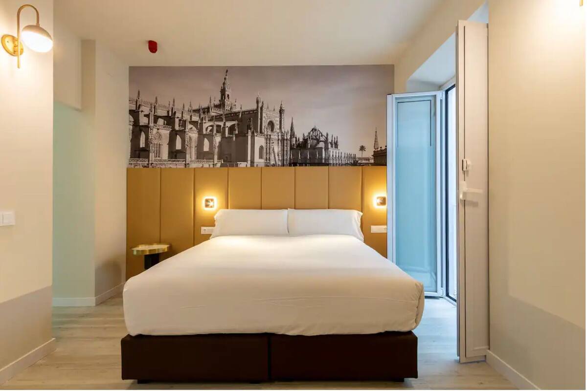 A bedroom with a large bed, a cityscape mural on the wall, and bedside lamps.