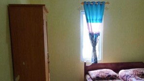 A bedroom with a bed, a wardrobe, a window with curtains, and an air conditioning unit. - Hotel O Wisma Nadira Near SPBU PT. Trijaya Pugung PENENGAHAN (Pesisir Utara)
