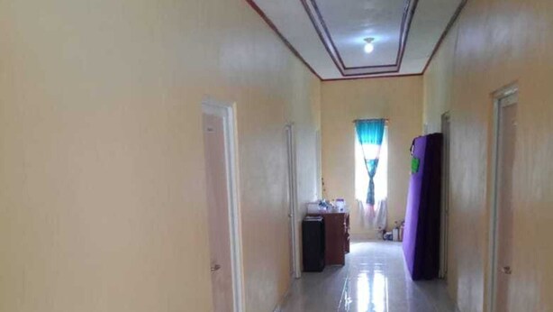 A long, narrow hallway with a tiled floor and cream-colored walls. - Hotel O Wisma Nadira Near SPBU PT. Trijaya Pugung PENENGAHAN (Pesisir Utara)