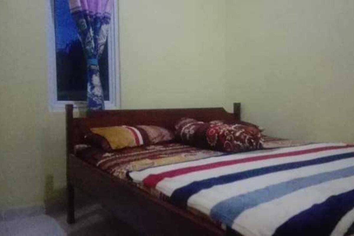 A single bed with a striped bedspread and multiple pillows in a room with plain walls and a window.