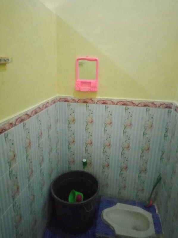 A small bathroom with a toilet, a bucket, and a pink mirror.