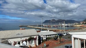 A coastal town with a marina, buildings with signage, and mountains in the background. - Studio apartment in the heart of Kalk Bay,  1 minute walk to the beach. (Cape Town)