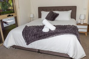 Relax in a spacious room with a large bed, two bedside tables, and a comfortable grey blanket.