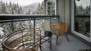 Varanda com cadeiras de vime e uma mesa, com vista para árvores e montanhas cobertas de neve.
