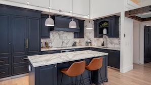Uma cozinha moderna com armários escuros, bancadas de mármore e iluminação pendente.