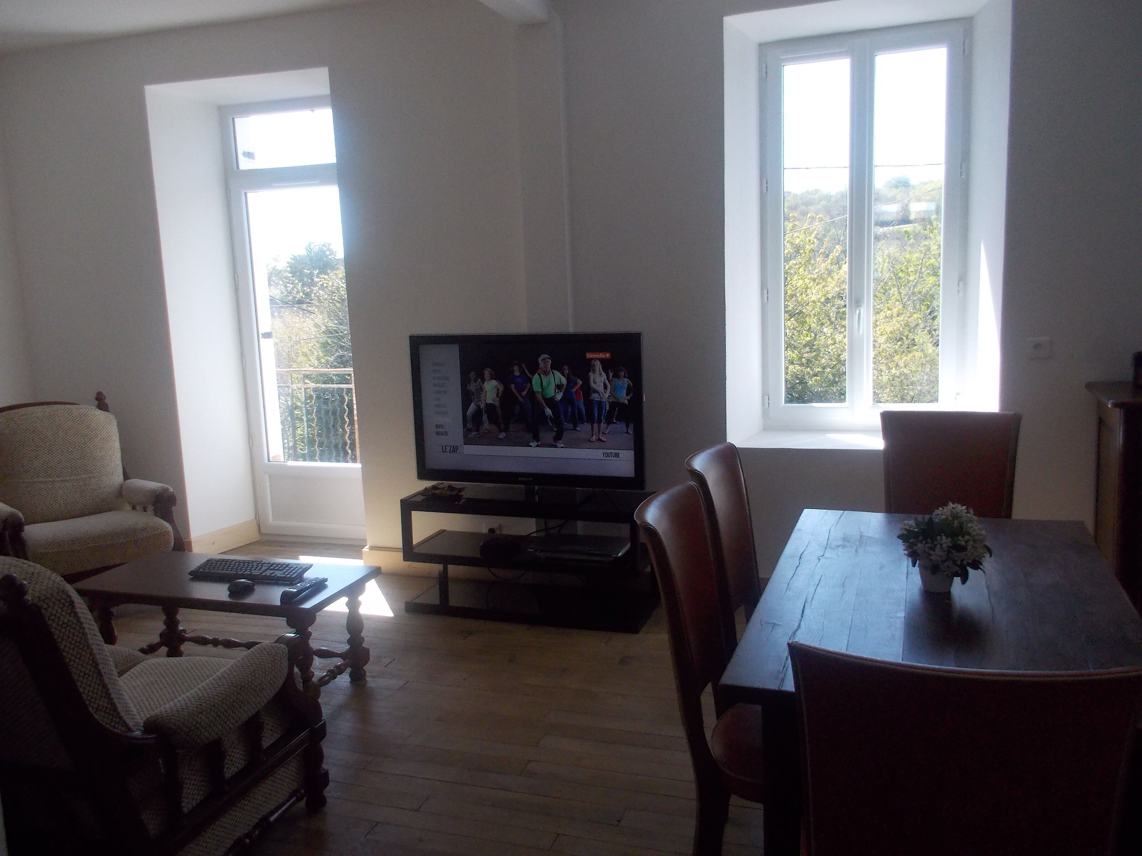 Ein Wohnzimmer mit Fernseher, Holzmöbeln und großen Fenstern.