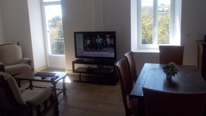 Ein Wohnzimmer mit Fernseher, Holzmöbeln und großen Fenstern.