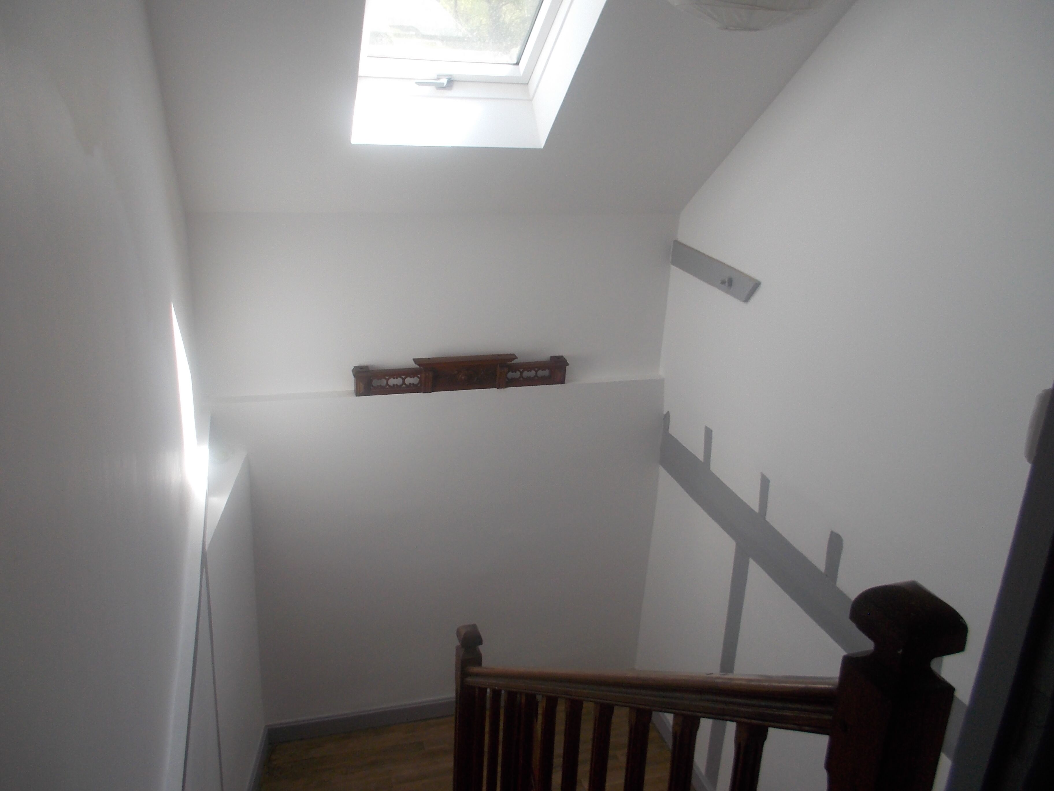 A narrow stairway with a wooden handrail, a skylight, and a small shelf with a box.