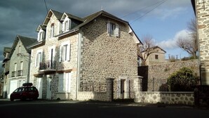 Ein Steinhaus mit Balkon und Garage, vor der ein rotes Auto parkt.