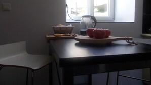 Eine Küche mit einem Holztisch, einem Korb, einem Wasserkocher und Tomaten auf einem Schneidebrett.