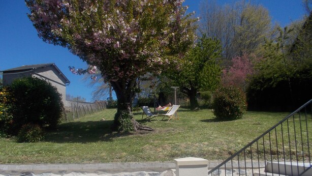 Eine Steintreppe führt zu einem Wohngebiet mit Rasen, einem Baum mit rosa Blüten und einem Haus im Hintergrund.