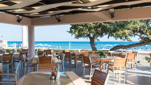 An outdoor dining area with tables and chairs, overlooking a beach and the sea. - Amaryllis Front Beach Hotel (Rhodes)