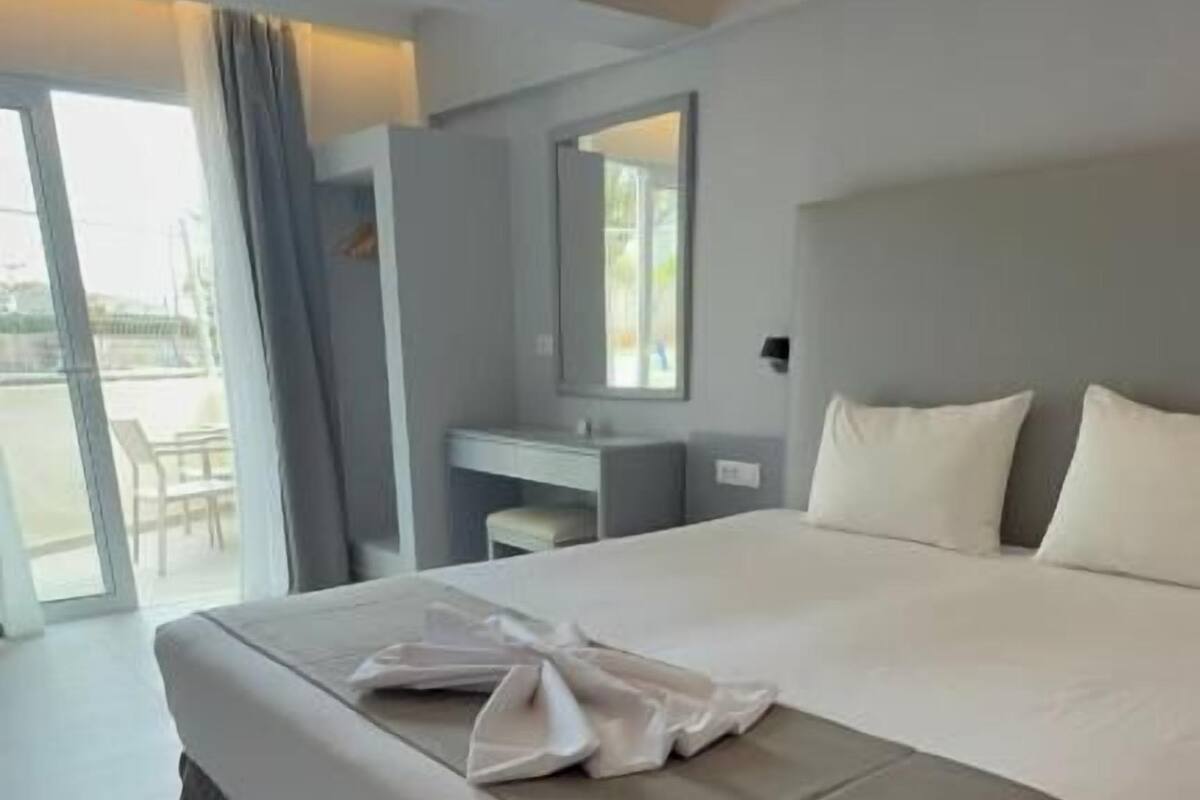 A modern hotel room with a large bed, a bedside table, a mirror, and a view of the outdoors.