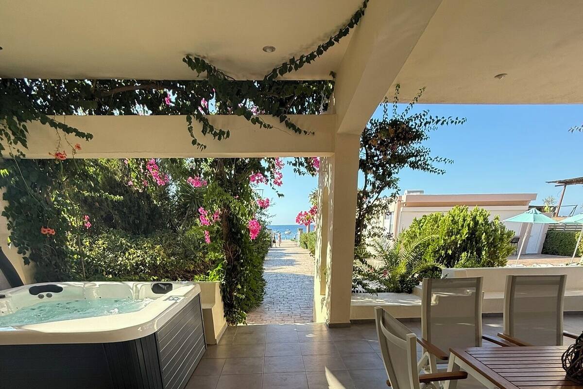 A covered outdoor area with a hot tub, chairs, and a view of the sea.