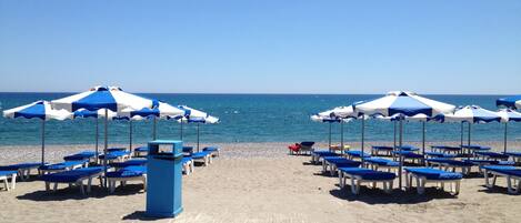 A beach with rows of blue and white beach umbrellas and lounge chairs facing the sea.