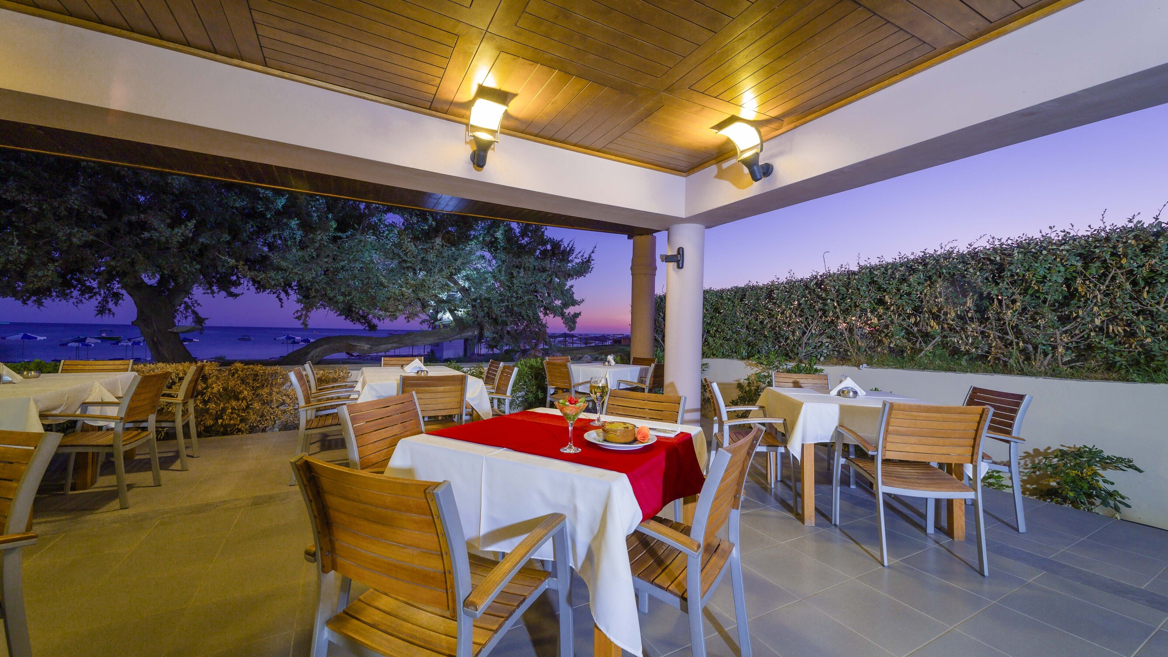 An outdoor dining area with tables and chairs, overlooking a body of water at dusk.