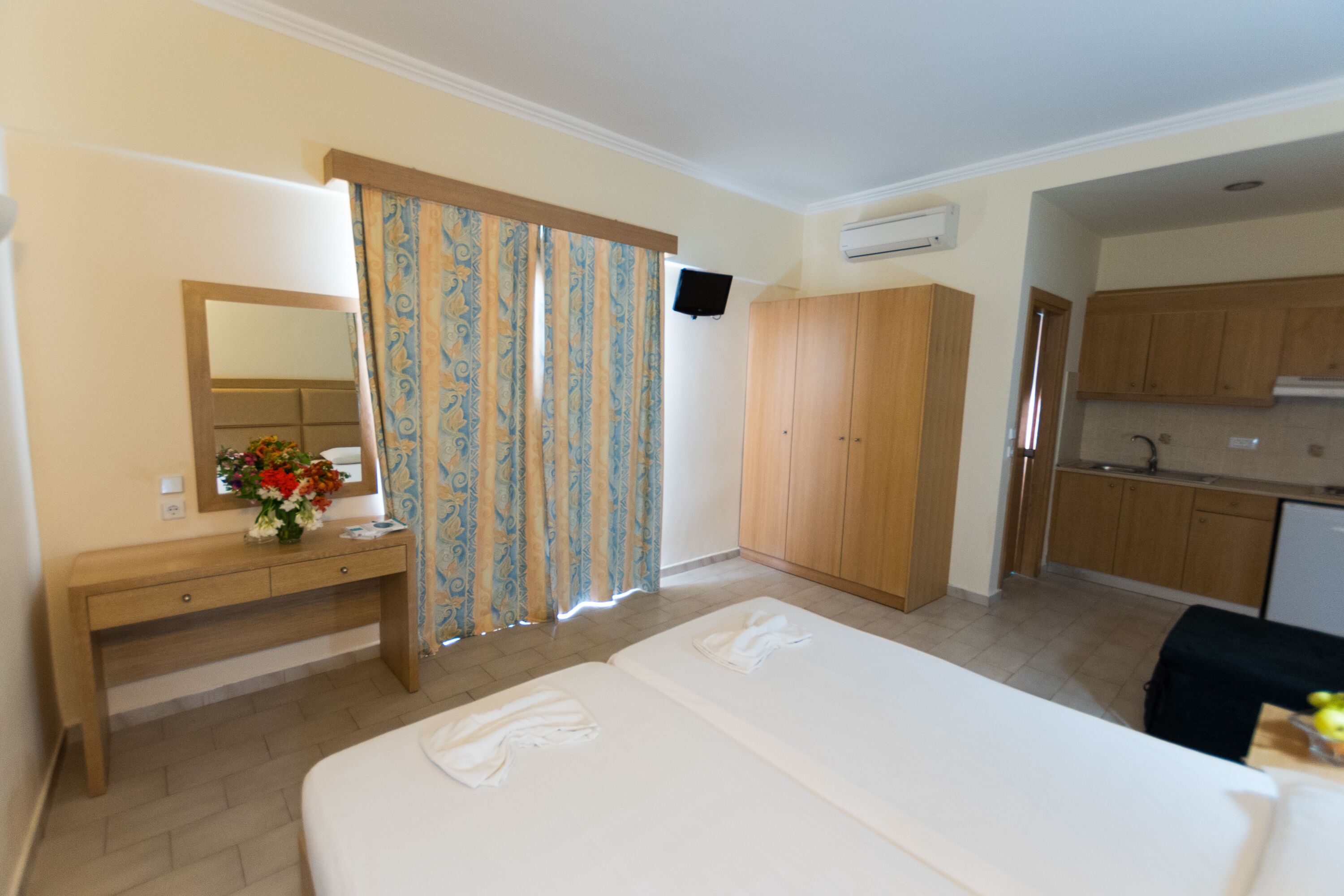 Ein Hotelzimmer mit einem Bett, einem Holzschrank, einem Schreibtisch mit Spiegel und einer kleinen Küchenzeile.