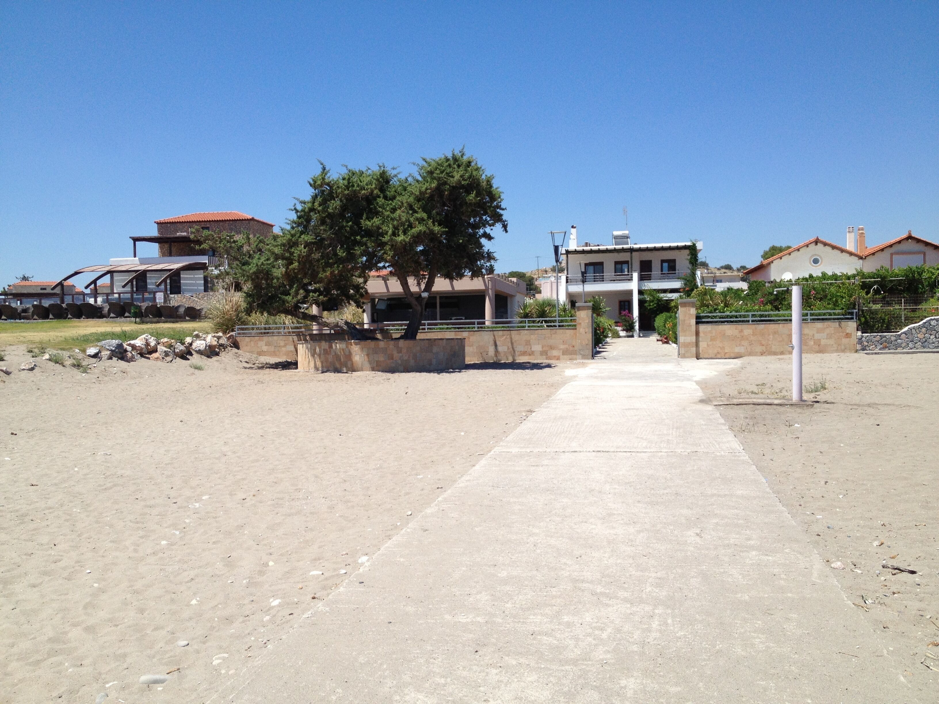 A pathway leading to a residential area with houses, a tree, and a clear sky.
