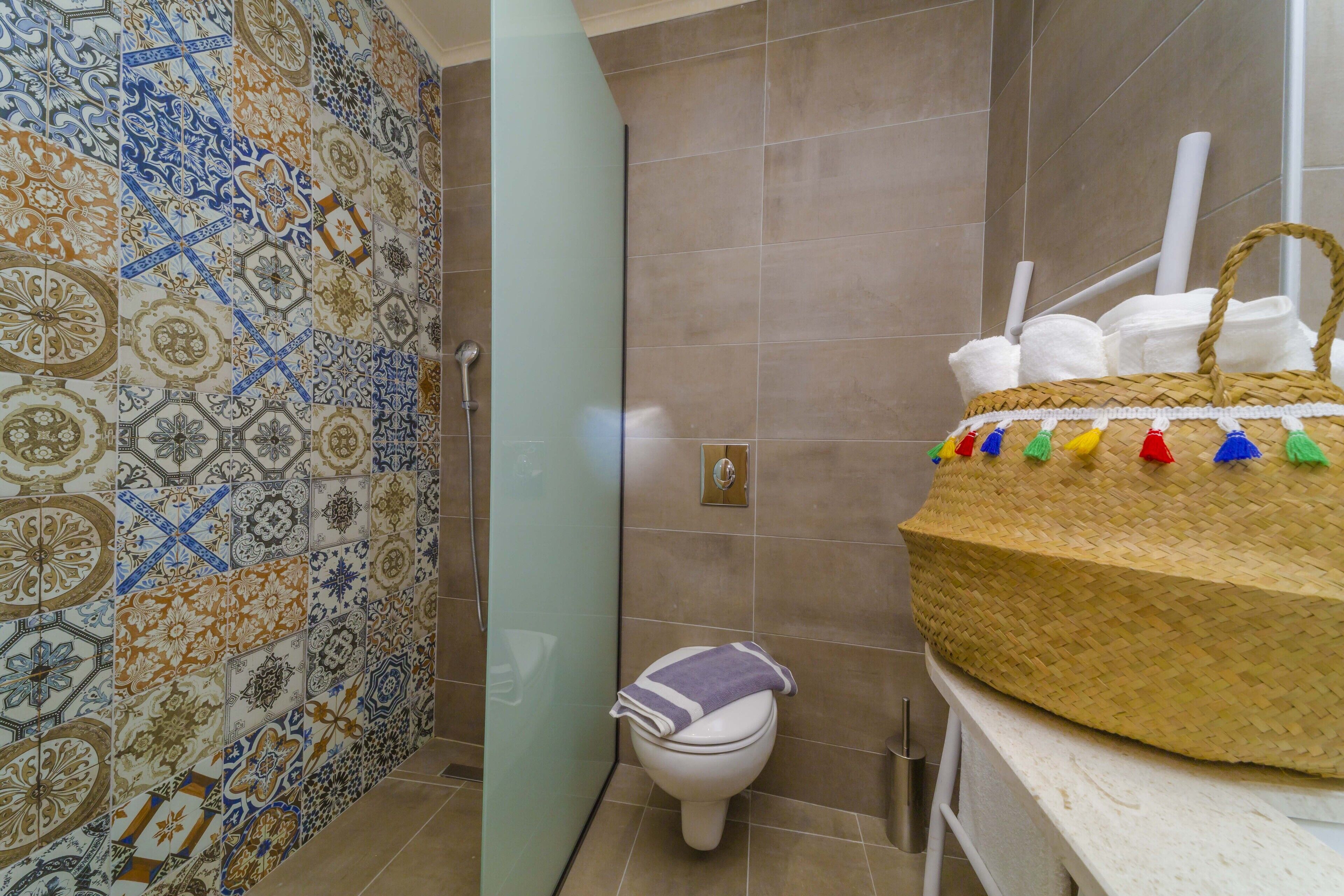 Ein Badezimmer mit gefliestem Duschbereich, Toilette und einem großen gewebten Korb auf der Ablagefläche.