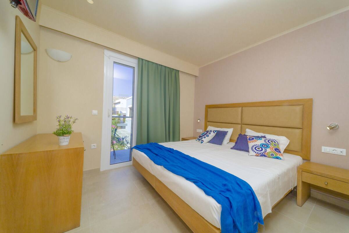 A bedroom with a bed, bedside table, and a small desk with a plant.