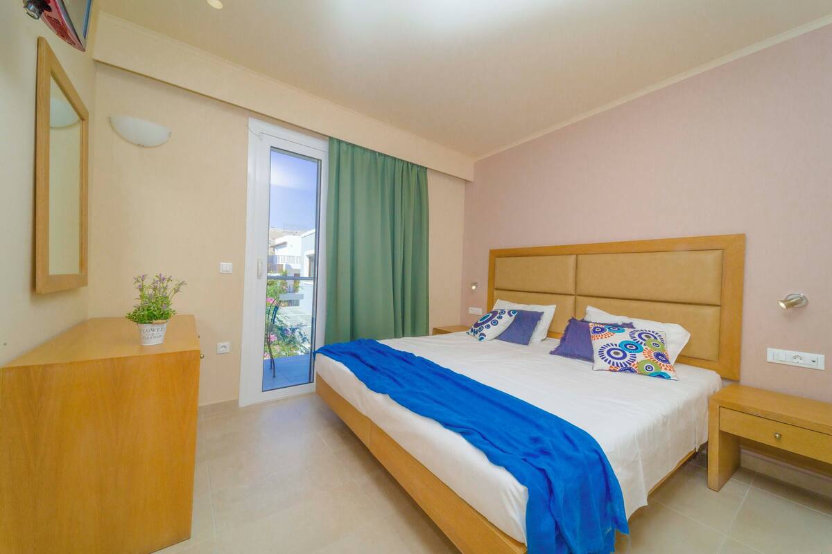 A bedroom with a bed, a nightstand, a dresser, a mirror, and a potted plant.