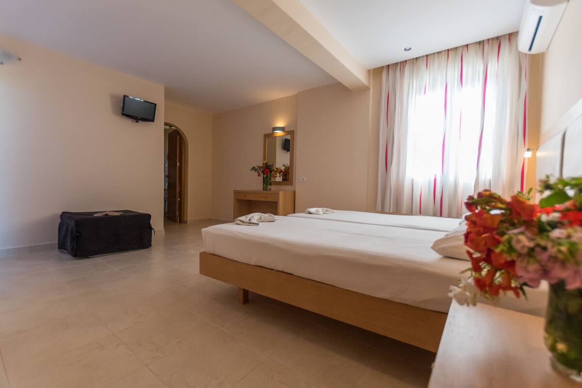 A hotel room with a bed, a desk, a mirror, a TV, and a suitcase.
