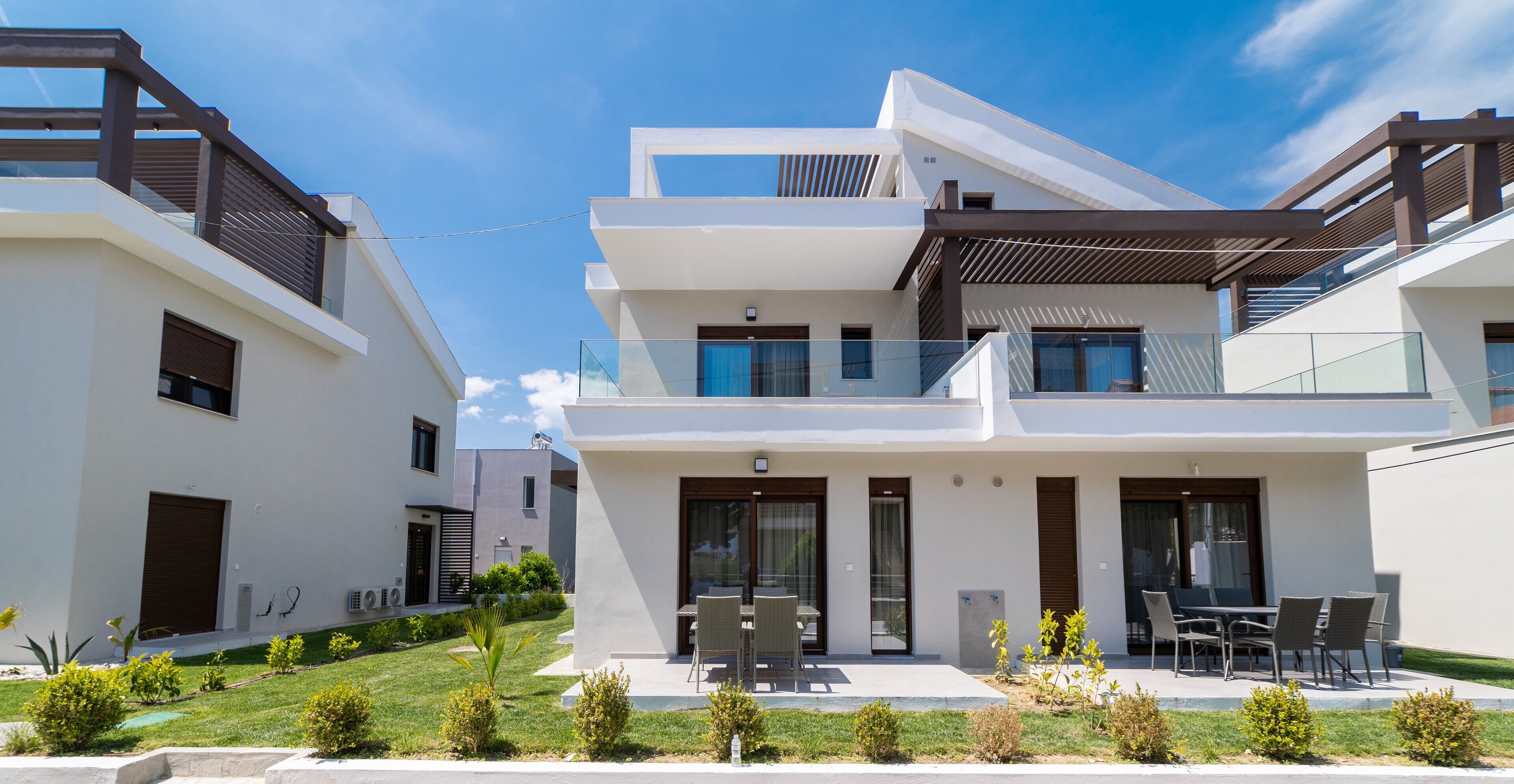 A modern two-story house with a balcony, a patio with outdoor furniture, and a well-maintained lawn.