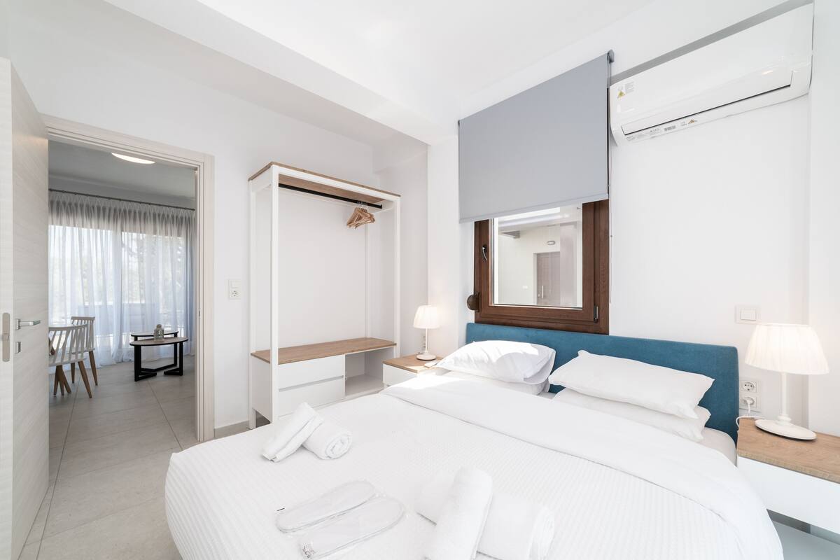 A modern hotel room with a large bed, bedside tables, a desk, a chair, and a wardrobe.